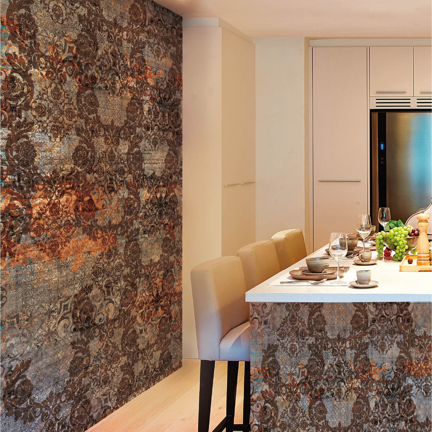 Angolo cucina con penisola. La parete laterale e il bancone sono rivestiti con una carta da parati damascata, in stile barocco e rovinato (effetto grunge), sui toni del marrone ruggine, grigio e arancione bruciato.